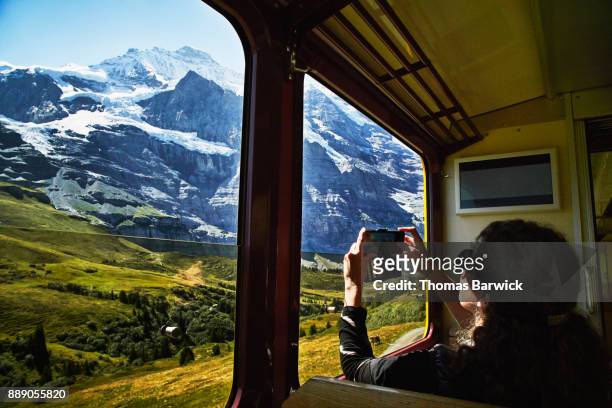 woman taking photo with smartphone of jungfrau while riding in train - zwitserland stockfoto's en -beelden