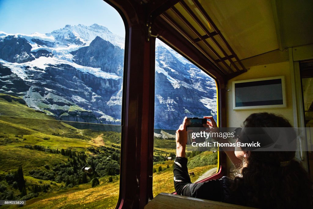 Woman taking photo with smartphone of Jungfrau while riding in train