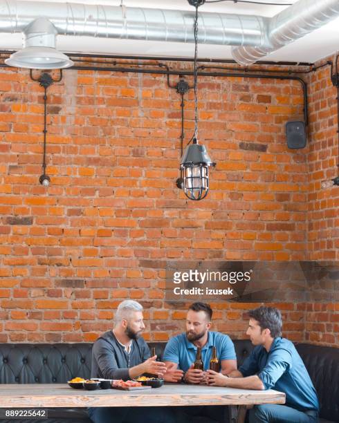 three friends meeting at pub after work - three people at table stock pictures, royalty-free photos & images