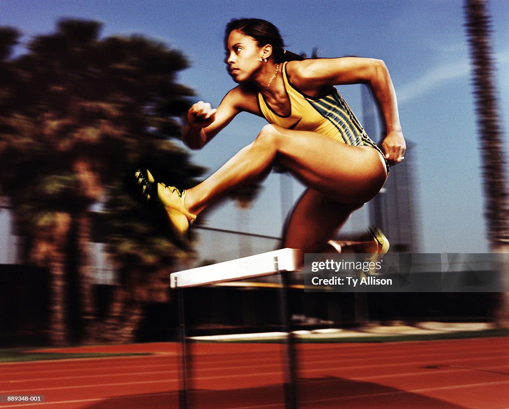 Female athlete jumping over hurdle, profile (blurred motion)