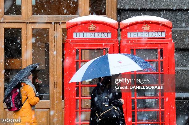 Pedestrians walk as snow falls over central London on December 10, 2017. Heavy snow fell across northern and central parts of England and Wales and...