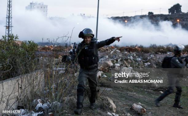 An Israeli border policeman gestures with his finger as he walks through tear gas fumes during clashes with Palestinian protesters near an Israeli...