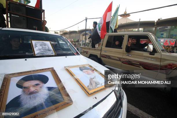 Members of the Hashed al-Shaabi flash the victory gesture as they drive past a pickup truck hanging on its hood portraits of Iraqi Shiite cleric...