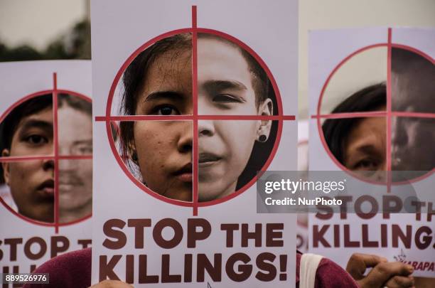 Human rights activists hold up posters with cutouts of crosshairs on one side and photos of extrajudicial killings on the other during the protest...