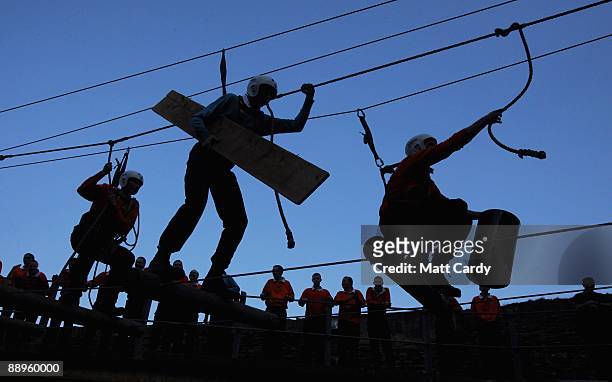 Royal Navy recruits try to cross a rope ladder laden with parts for a raft above water in the harbour at the Piers Cellars training centre as they...