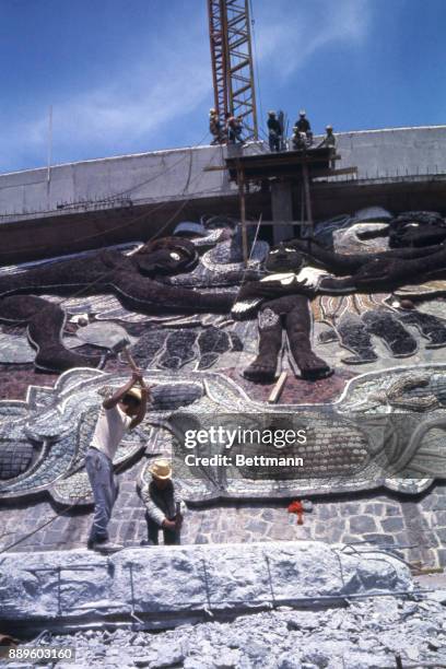 Workmen erect pedestal for the Olympic torch above a mosaic on the side of the Olympic Stadium at the University of Mexico. Torch will be lighted...