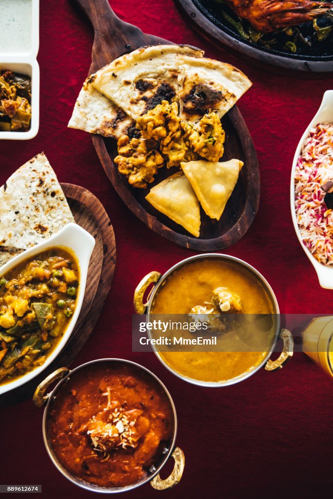 A festa indiana com frango manteiga, frango tandoori, cordeiro ao curry, caril de vegetal, chamuças, pakoras, bhajis, pão naan e basmati arroz sobre uma mesa. Comida indiana do Norte