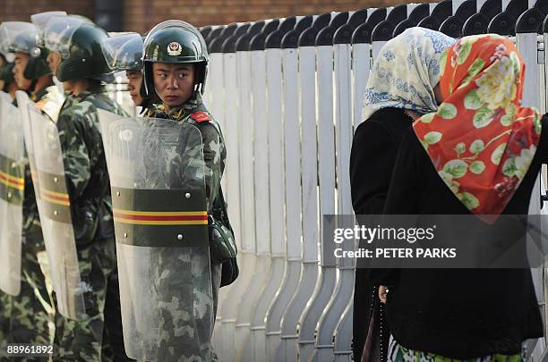 An ethnic Uigur women look through a security fence to the Grand Bazaar which remains closed as Chinese soldiers look on in Urumqi, in China's...