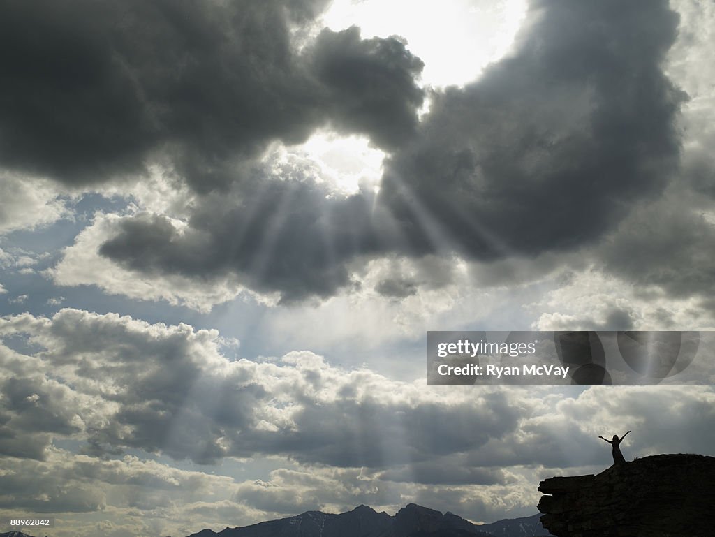 Woman standing on cliff, arms outstretched