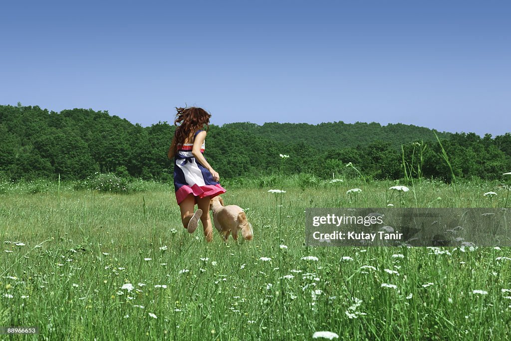 Young girl and dog running in field.