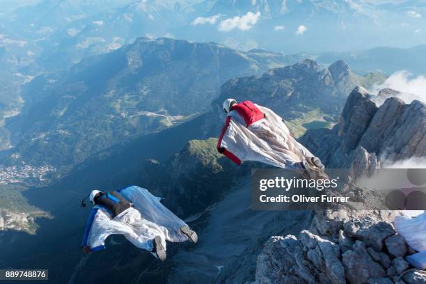 wingsuit base jumpers exited from a cliff and are proximity flying together downwards into the valley. - base jumping imagens e fotografias de stock