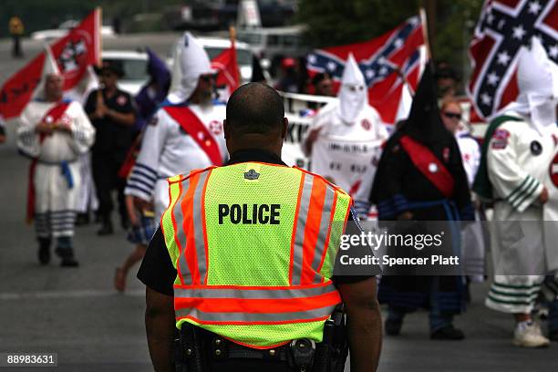 Police officer watches as members of the Fraternal White Knights of the Ku Klux Klan participate in the 11th Annual Nathan Bedford Forrest Birthday...