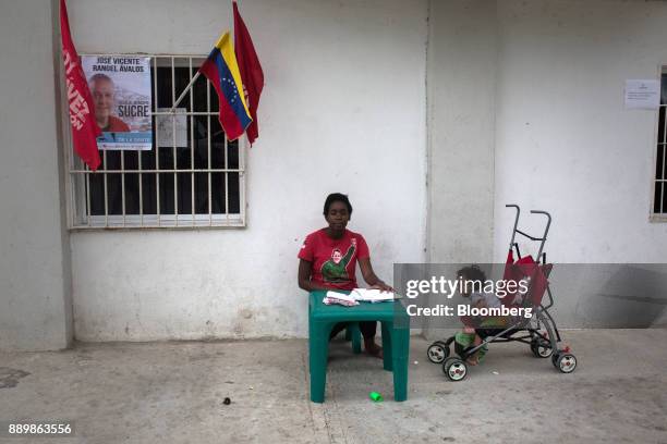 An electoral official wearing a t-shirt displaying the image of late Venezuelan president Hugo Chavez sits at a checkpoint outside a polling station...