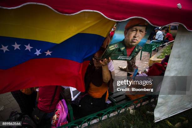 An electoral official looks past a Venezuelan flag and an image of late Venezuelan president Hugo Chavez at a checkpoint outside a polling station...