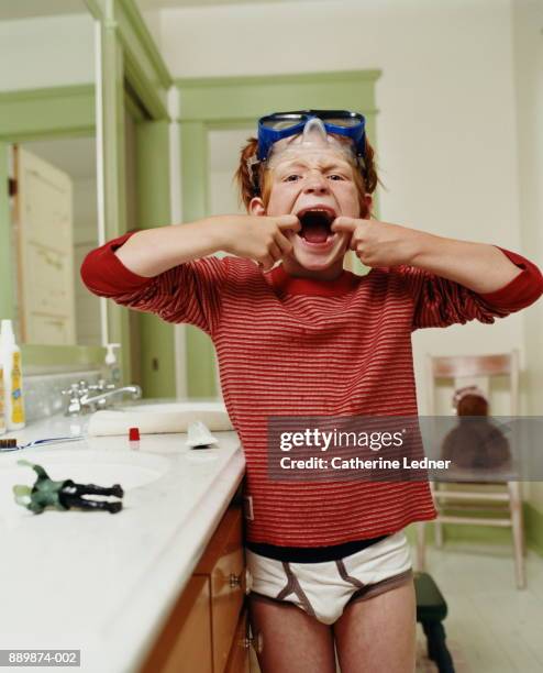 boy (6-8) pulling mouth after brushing teeth, goggles on head - ungezogenes kind stock-fotos und bilder