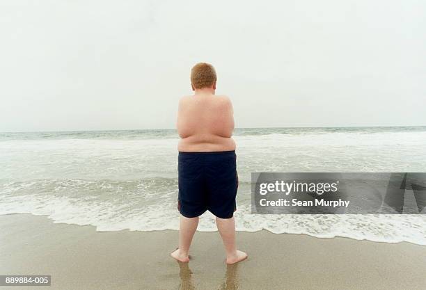 overweight boy (10-12) standing on beach, rear view - fat redhead stock pictures, royalty-free photos & images