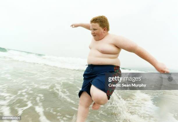 boy (10-12) jumping over waves on beach - fat redhead fotografías e imágenes de stock