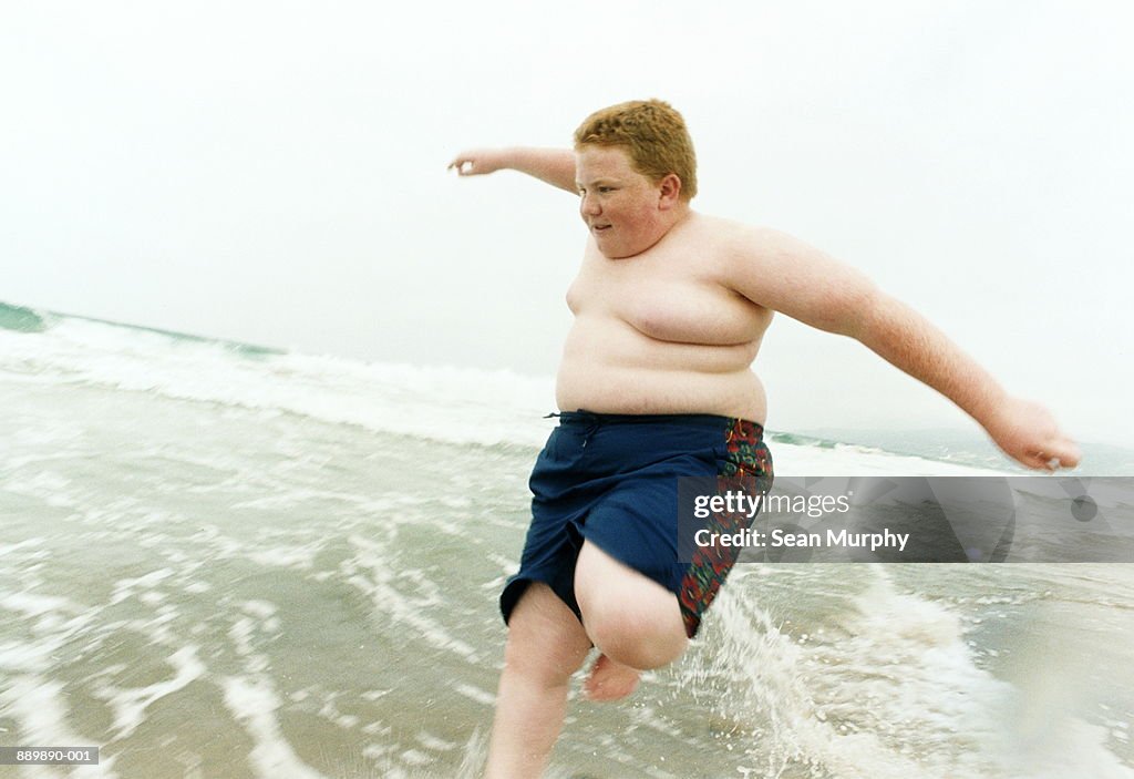 Boy (10-12) jumping over waves on beach