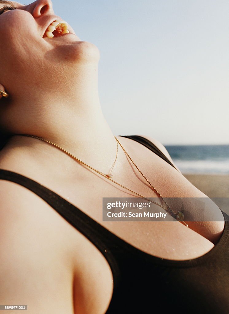 Woman in black swimsuit laughing on beach