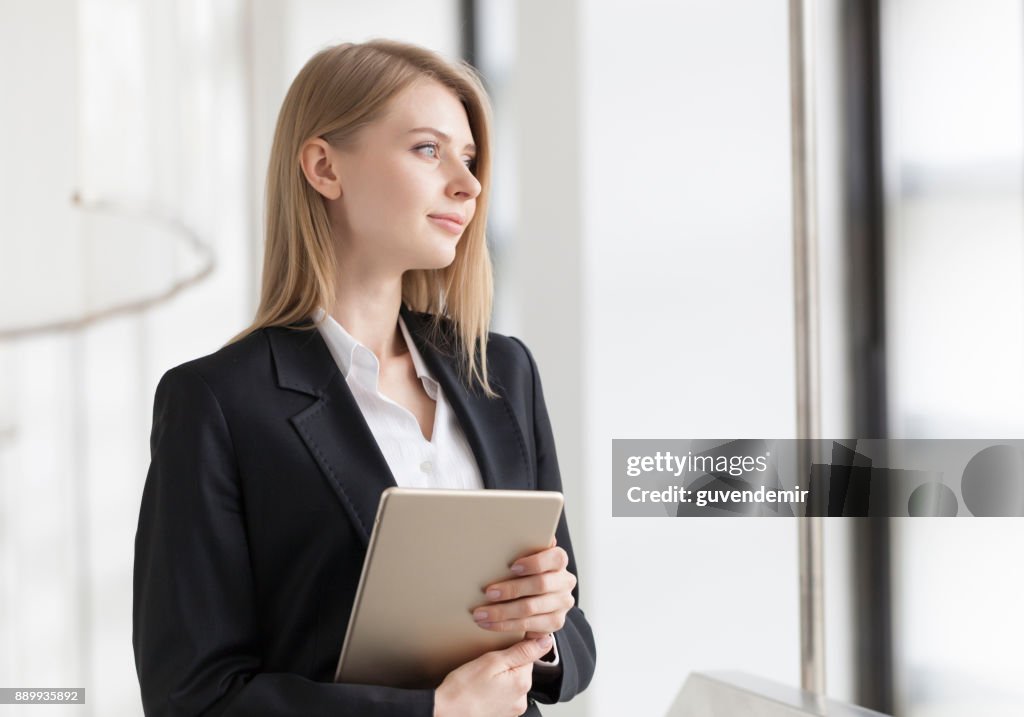 Cheerful young businesswoman standing with digital tablet