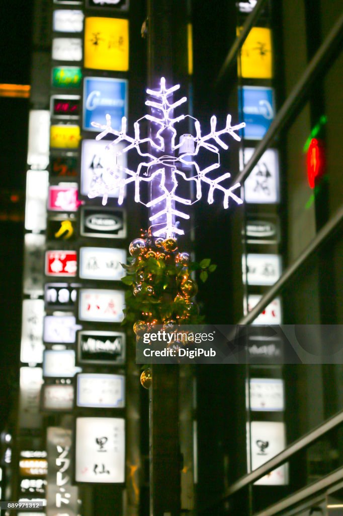 Snowflake shaped Christmas lights against sign boards and neon on Konbaru Dori Street in Ginza