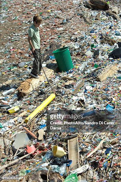 boy standing in garbage dump, garbage can nearby, high angle view - sinnlosigkeit stock-fotos und bilder