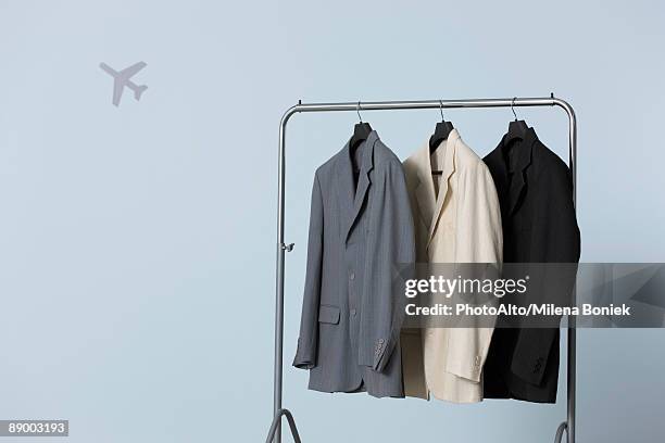 three men's suit jackets hanging on clothes rack, airplane shape in background - clothes rack stock-fotos und bilder