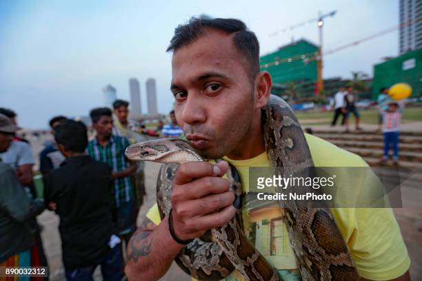 Sri Lankan man wraps a full-grown pet python reptile on his neck and kisses it at one of the more popular recreation spots, the Galle Face Green in...