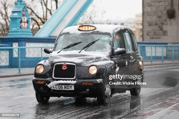 Snow covered black cab taxi travels across Tower Bridge during a snow shower on December 10th, 2017. Much of the UK has been hit by heavy snow and...