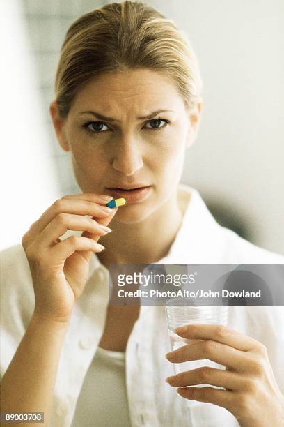 woman holding pill, frowning at camera - knitting brow stock pictures, royalty-free photos & images
