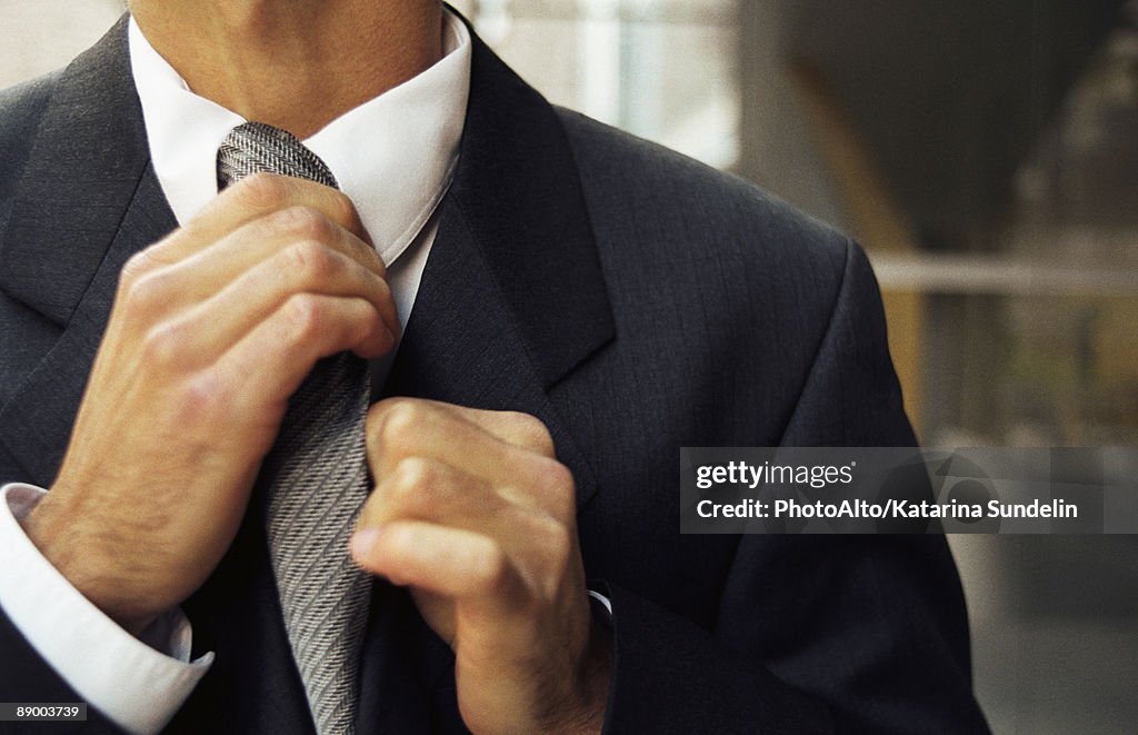 Man adjusting tie, cropped