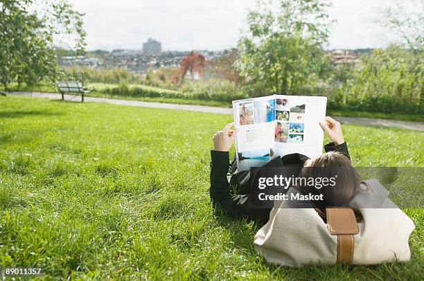 woman lying on lawn reading a magazine - magazine reading stock pictures, royalty-free photos & images