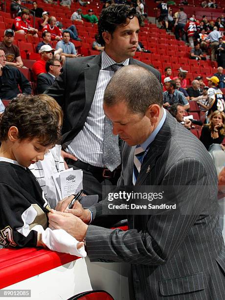 Assistant Coach Tom Fitzgerald of the Pittsburgh Penguins signs an autograph for a young hockey fan as former NHL player Travis Green looks on from...