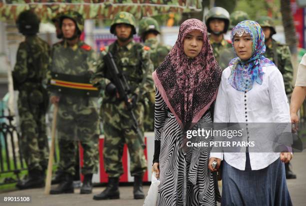 Two ethnic Uighur women pass Chinese paramilitary policemen standing guard outside the Grand Bazaar in the Uighur district of the city of Urumqi in...