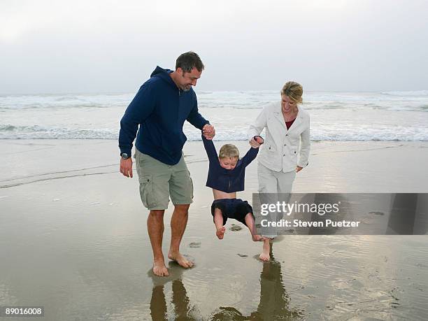 parents swinging boy by hands on beach - lincoln city oregon stock pictures, royalty-free photos & images