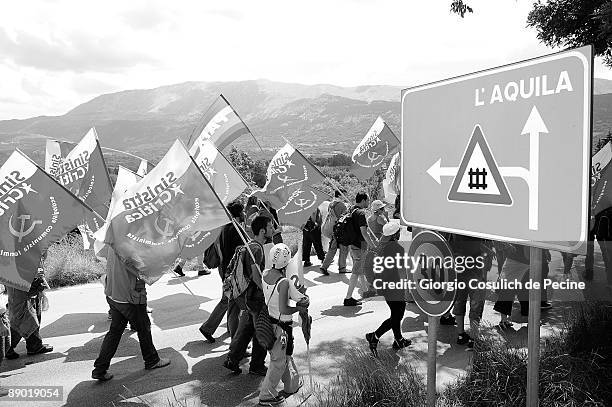 Crowd of demonstrators holding flags walk past a road sign towards L'Aquila during a protest against the G8 summit on the third day of the...