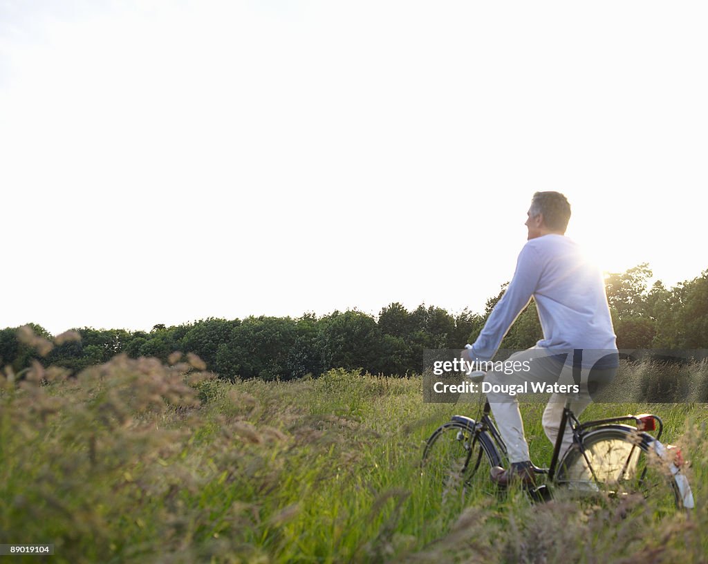 Man riding bike through countryside meadow.