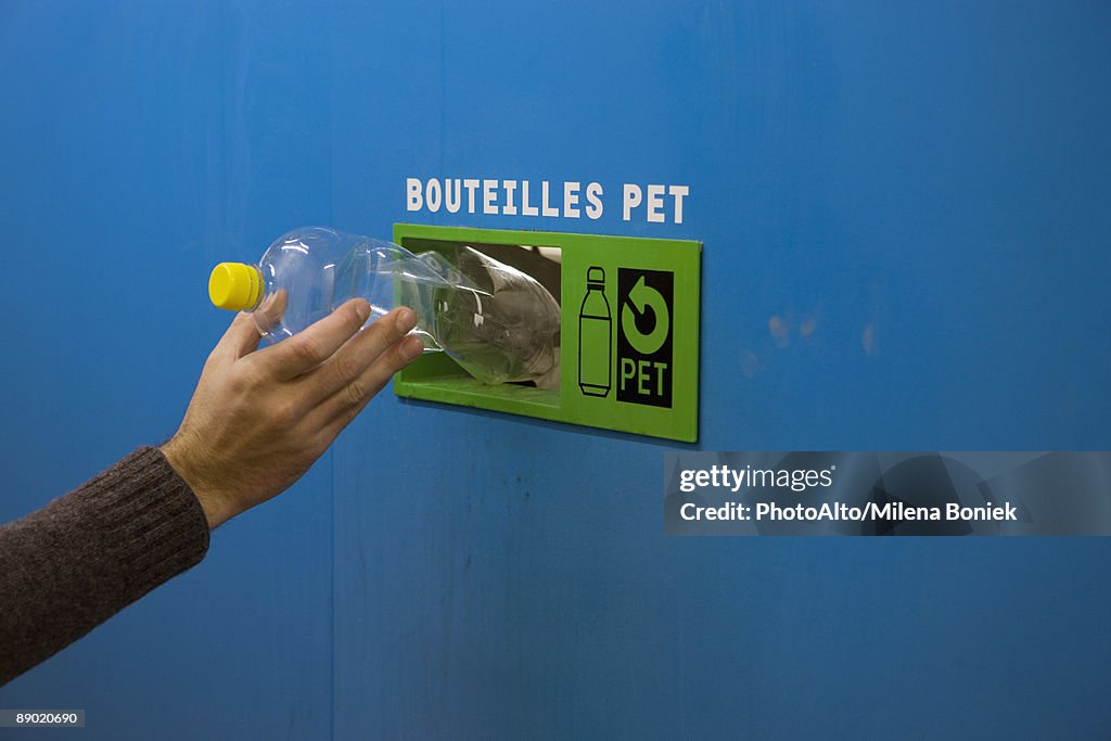 Person placing plastic bottle in recycling receptacle, cropped view