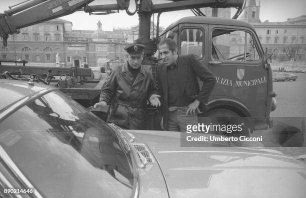 Adriano Celentano with the traffic policemen while they take away the car parked in a no parking area, Rome 1976. Adriano Celentano is a famous...
