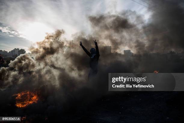 Palestinian youth gestures in the smoke of a tire fire as they clash with Israeli Defence Forces in the streets on December 11, 2017 in North of...