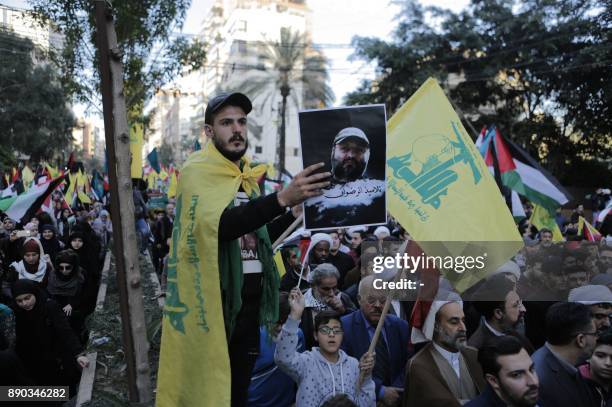 Lebanese Shiite protester, draped in a Hezbollah flag holds up a portrait of the Shiite movement's slain former military commander Imad Mughniyeh,...
