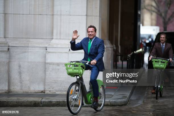 Former Governor of the US State of California Arnold Schwarzenegger waves as he rides a bicycle in Paris on December 11 on the sidelines of meetings...