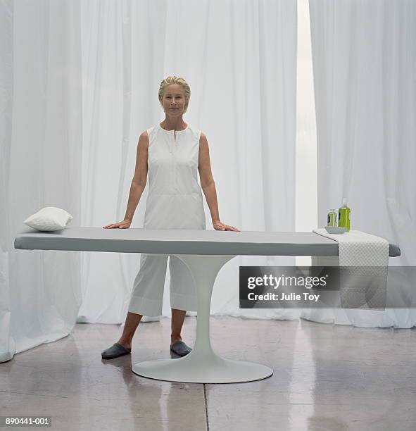 mature woman in white standing next to massage table - banc de massage photos et images de collection