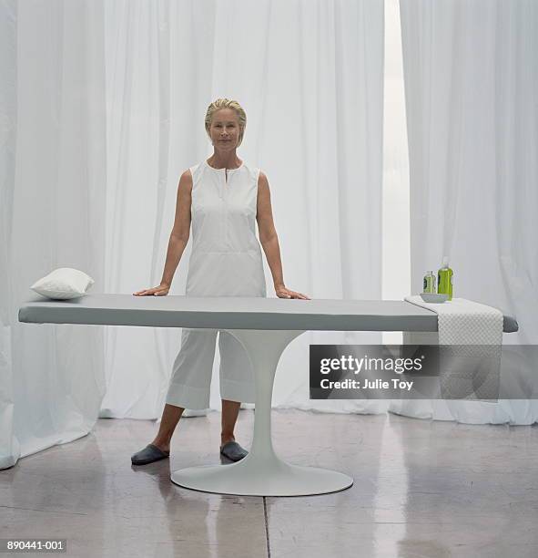 mature woman in white standing next to massage table - massage table imagens e fotografias de stock