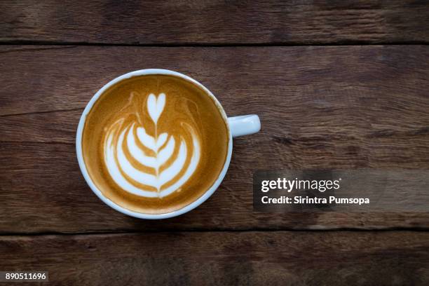 a white cup of hot latte art coffee on the wooden table in coffee shop - coffee top view stock-fotos und bilder