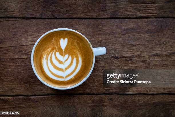 a white cup of hot latte art coffee on the wooden table in coffee shop - coffee art stockfoto's en -beelden