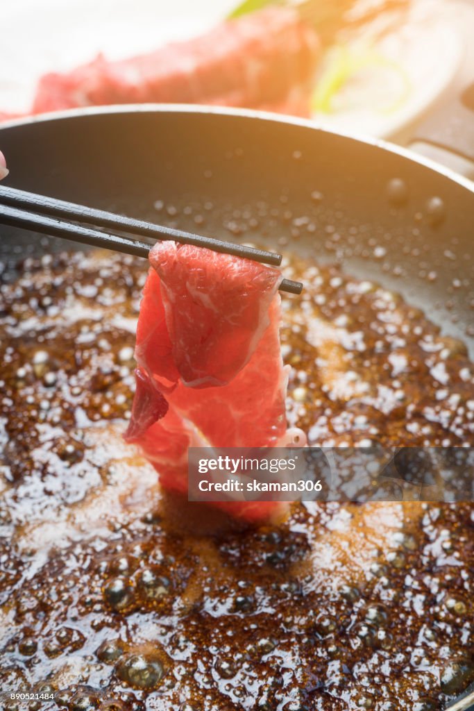 Black chopstick holding raw wagyu beef