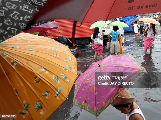 Filipino schoolchildren and their parents maneouver through a flooded street following heavy downpours in suburban Malabon city north of Manila July...