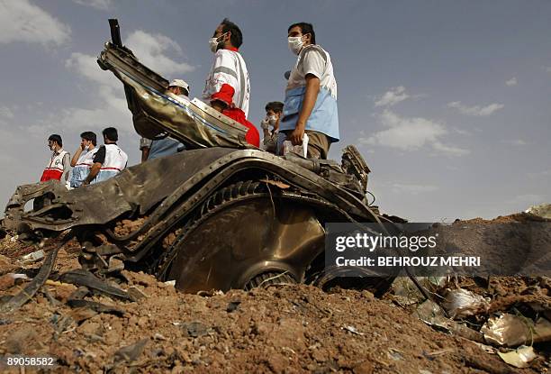 Members of Iran's Red Crescent stand near a piece of the Caspian Airlines Tupolev-154, which crashed on July 15 near the city of Qazvin, northwest of...