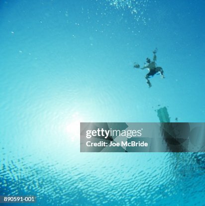Man jumping off diving board into water, underwater view Man jumping off diving board into water, underwater view